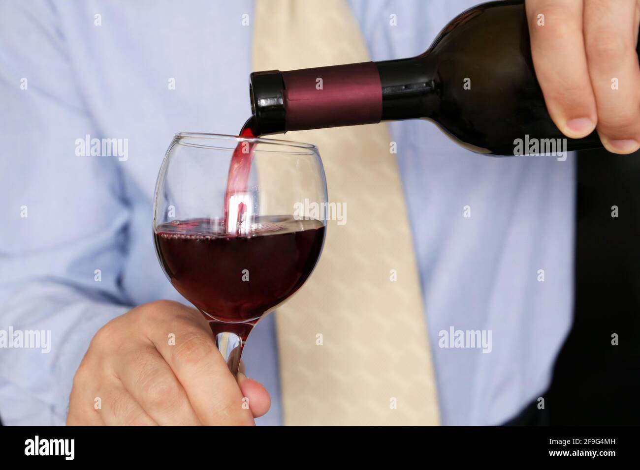 Uomo in abiti da lavoro che versa vino rosso in un bicchiere dalla bottiglia. Festa aziendale in ufficio, cena romantica in un ristorante Foto Stock