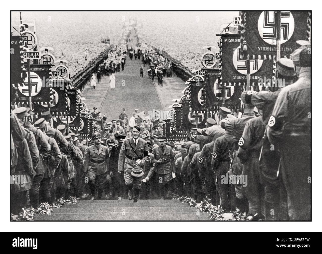 Adolf Hitler degli anni '30, dittatore tedesco nazista Fuhrer, salendo i gradini a Buckeberg, per una cerimonia annuale del Ringraziamento del Reich nel 1933-1937, affiancata da sturmabteilung, che trasportano bandiere di bandiere di striscioni di bandiere swastika naziste Foto Stock