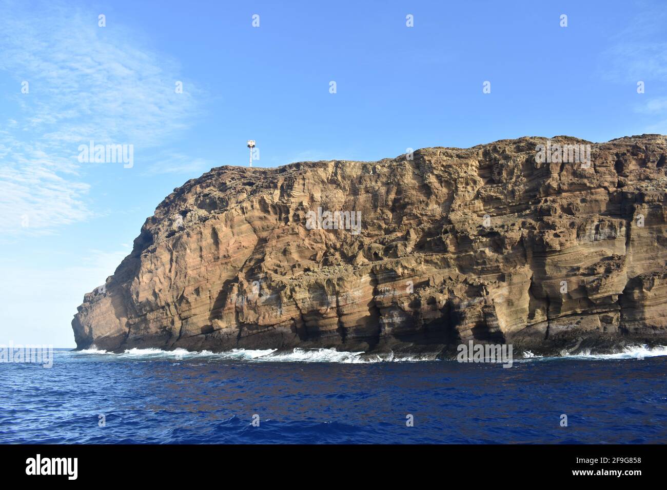 La roccia del Cratere Molokini dall'Oceano Pacifico, montagna sullo sfondo, Isola Hawaiiana di Maui Foto Stock