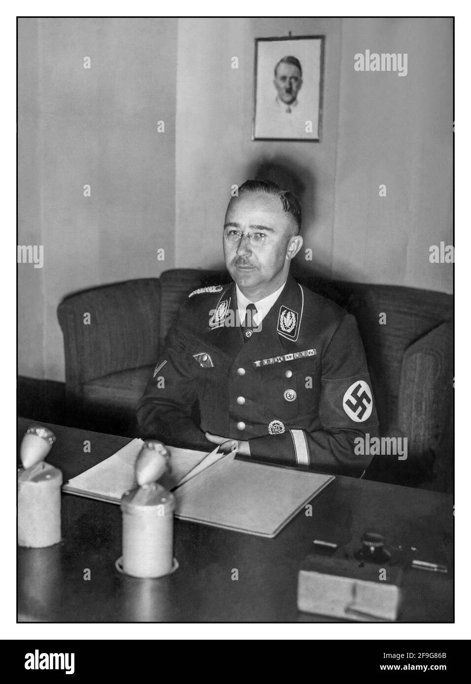WW2 1939 Heinrich Himmler nella sua divisa nazista alla sua scrivania di Berlino facendo una trasmissione radiofonica propagandistica alla popolazione nazista della Germania. Ritratto di Fuhrer Adolf Hitler alle spalle Foto Stock