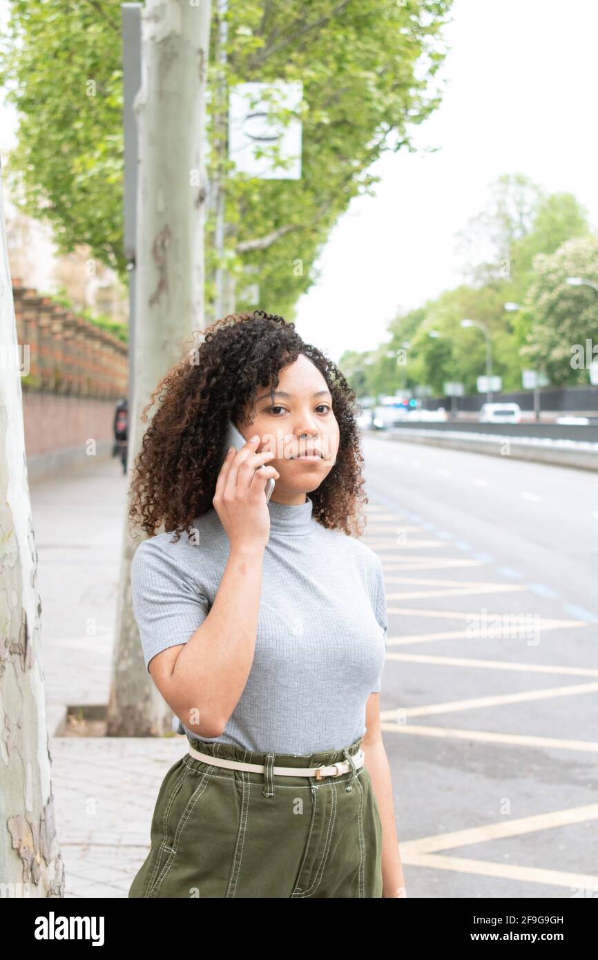 Donna nera con capelli ricci che chiama un taxi in città su un cellulare. Foto Stock