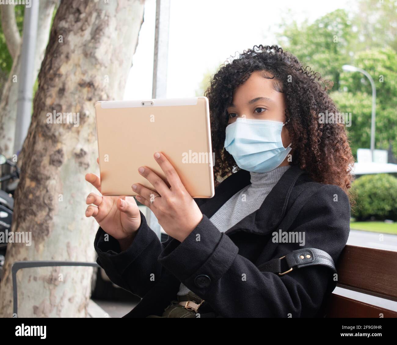 ragazza nera con capelli ricci che indossa una maschera e una tavoletta all'aperto. Foto Stock