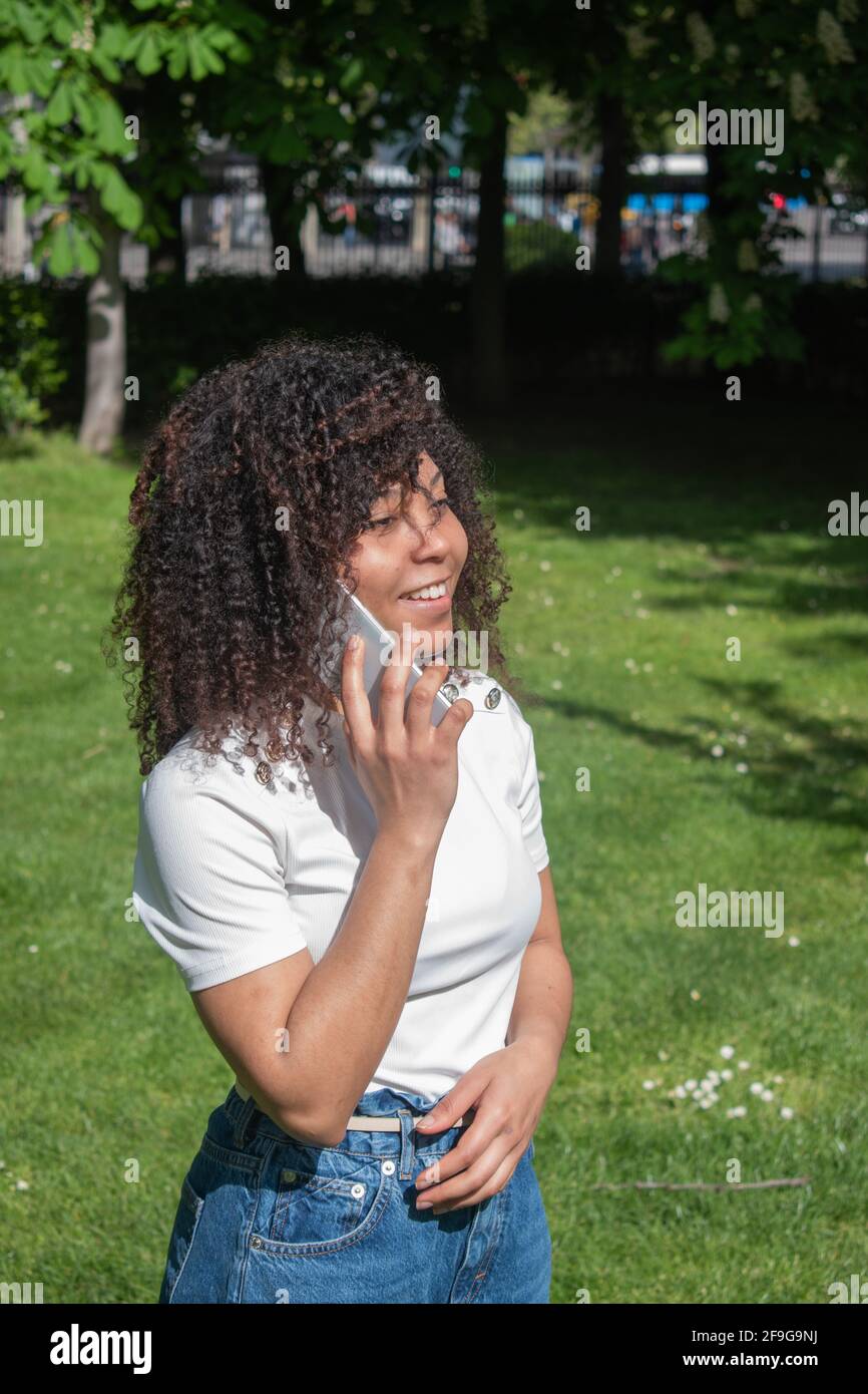 Donna con capelli ricci che parla al telefono in un area naturale Foto Stock