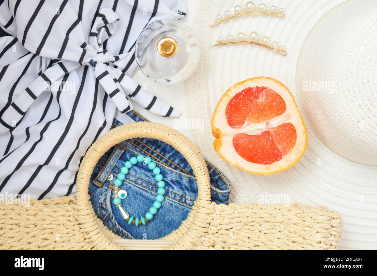 braccialetto in turqouise a righe e pompelmo rosso succoso su sfondo bianco. abiti estivi per stile di vita femminile, flatlay Foto Stock