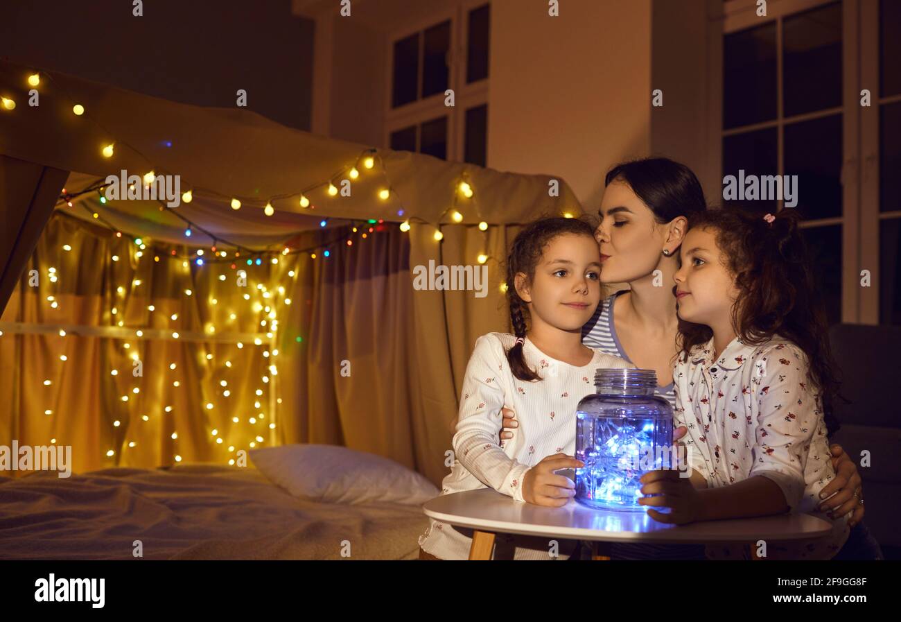 La madre caucasica bacia i bambini sulla fronte prima di andare a dormire in un ambiente accogliente camera da letto in casa Foto Stock