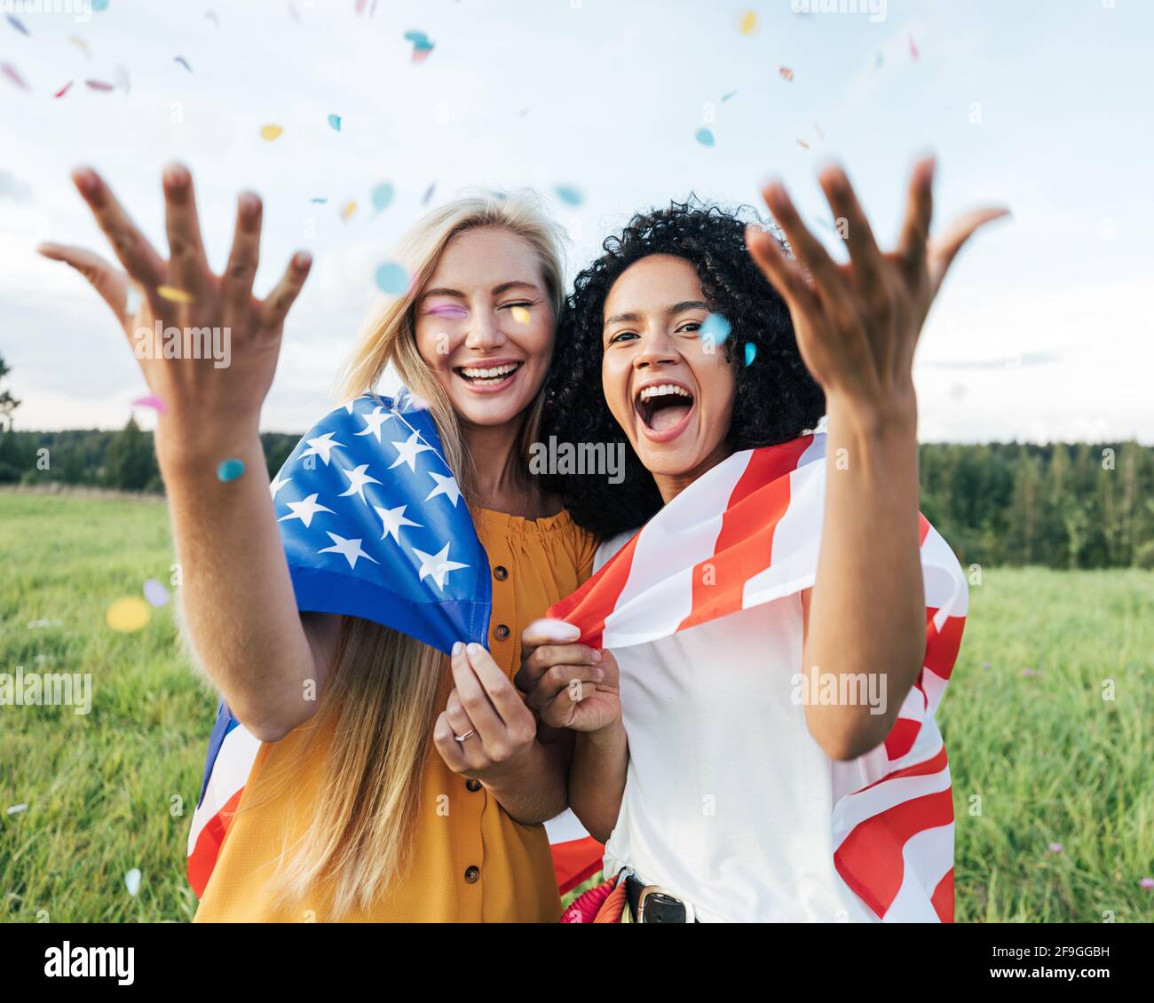 Due amiche ridenti che gettano i confetti nell'aria mentre in piedi su un campo Foto Stock