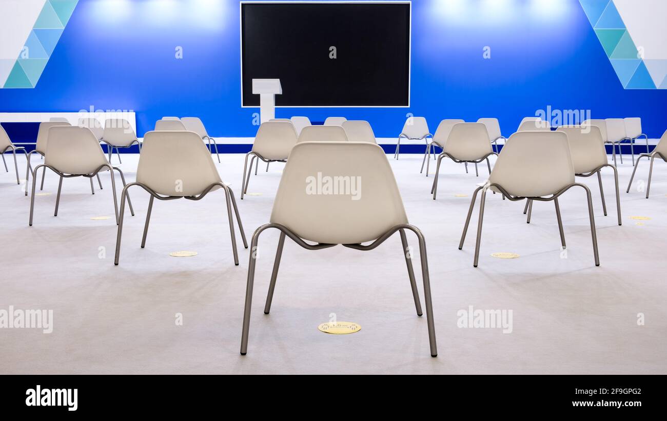 Super sala conferenze con sedie bianche e illuminazione colorata e schermo vuoto, distanza sociale Foto Stock