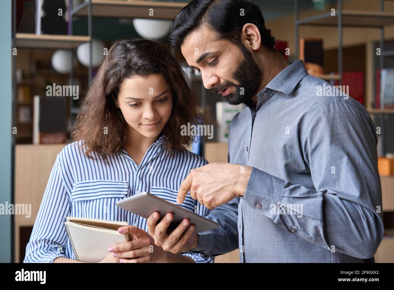 Responsabile indiano e giovane dipendente latino che parla in ufficio utilizzando un dispositivo tablet. Foto Stock