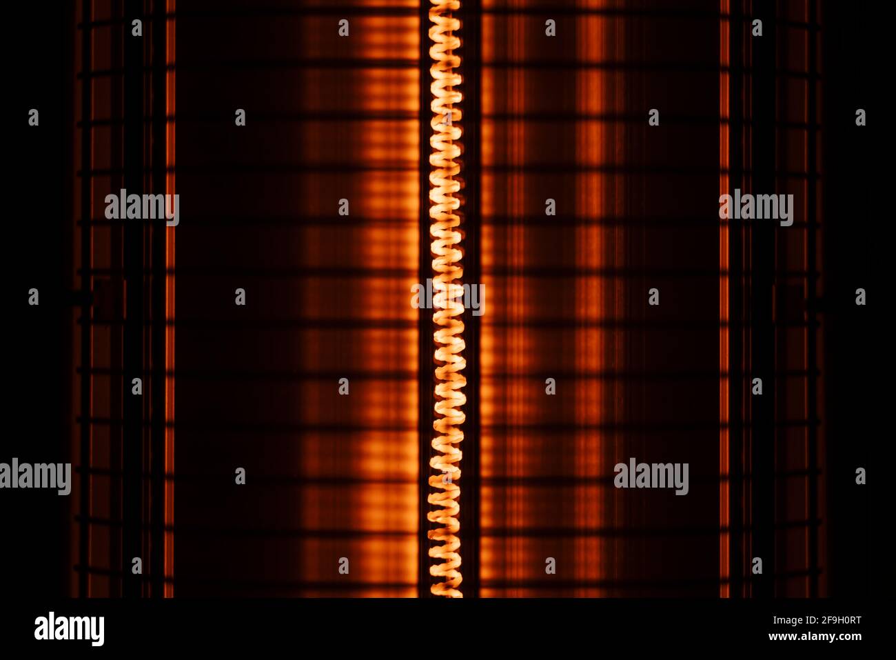 Primo piano di una bobina del riscaldatore elettrico arancione rossa con protezione griglia Foto Stock