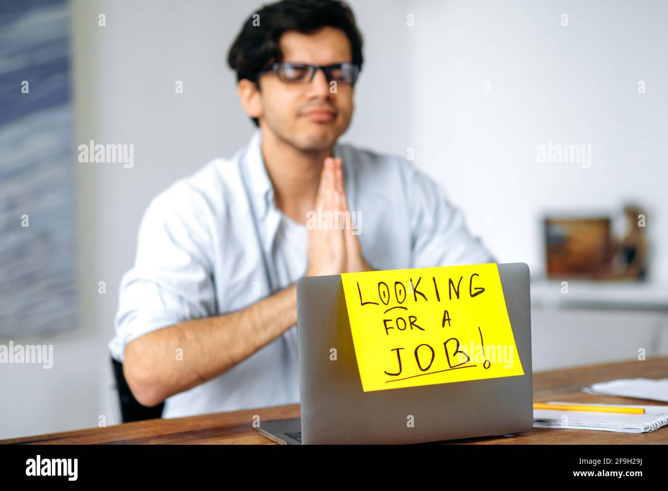 Un ragazzo intelligente, studente o disoccupato, si siede a un tavolo, alla ricerca di un lavoro sulla rete, guarda gli annunci, spera di ottenere un lavoro da sogno, su un laptop un segno con l'iscrizione alla ricerca di un lavoro Foto Stock