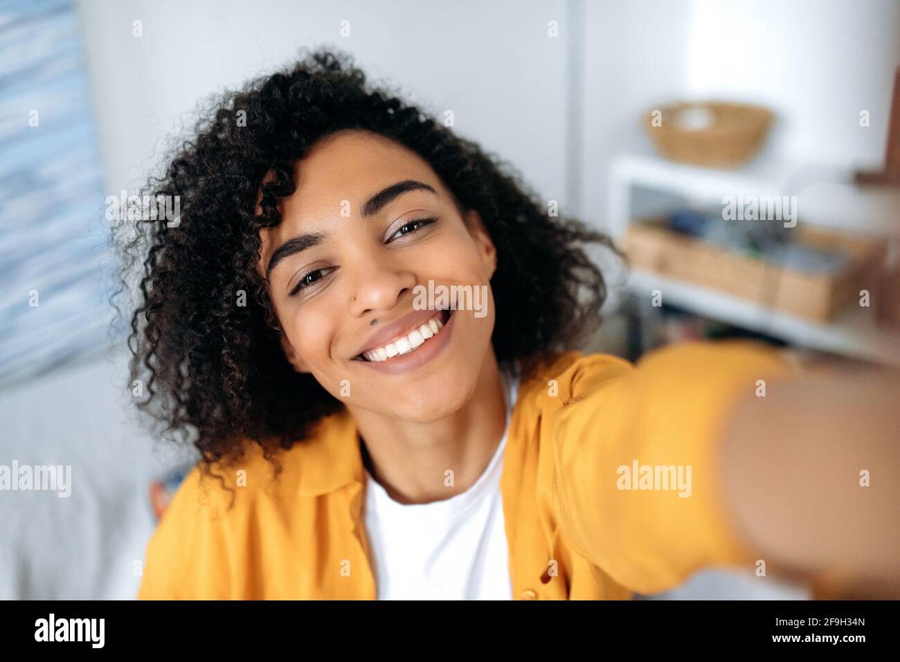 Selfie foto sullo smartphone. Gioioso spensierato curly afroamericano ragazza, studente, freelance, fa un selfie al telefono, imbrogliando intorno, divertendosi, guarda la webcam del telefono, sorridere felicemente Foto Stock