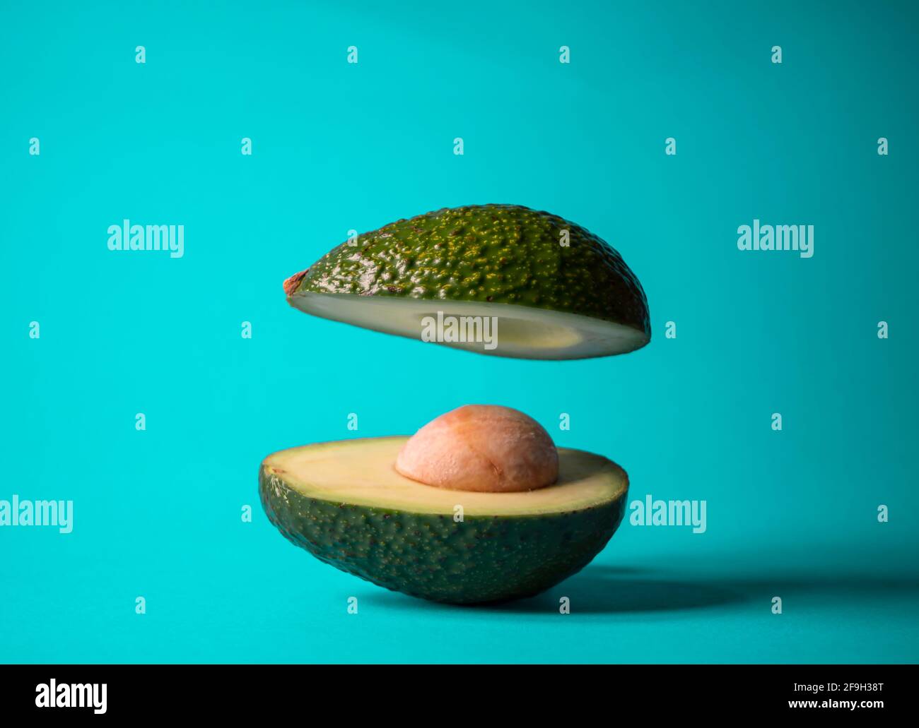 Frutta galleggiante all'avocado tagliata a metà su sfondo acquamarina. Concetto minimo di natura. Vibrazioni estive. Idea di cibo sano. Foto Stock