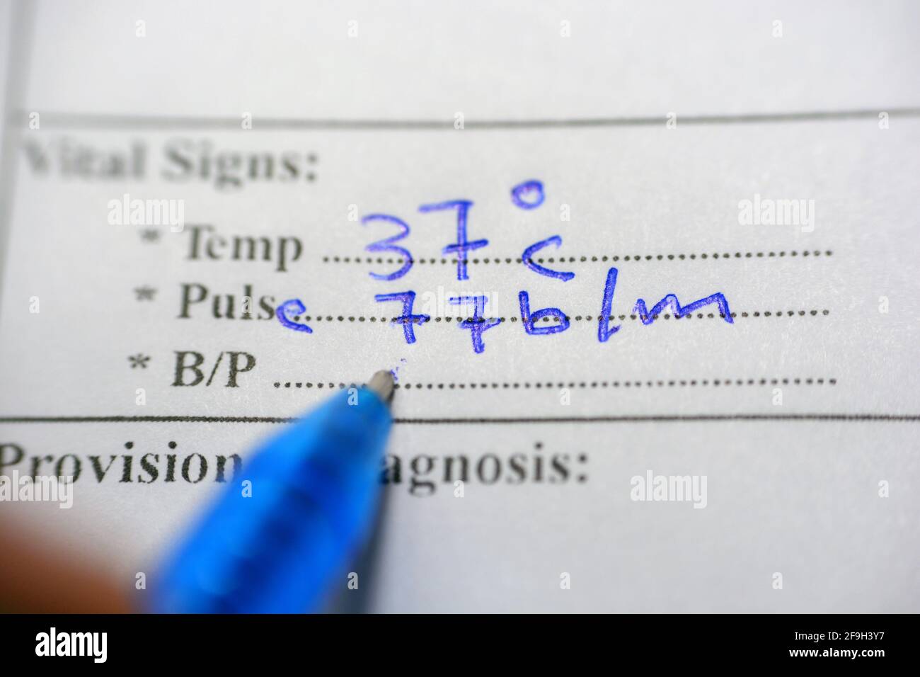 Il personale medico scrive i dati vitali (temperatura corporea, polso e pressione sanguigna) di un paziente che segue il suo caso in una cartella clinica Foto Stock