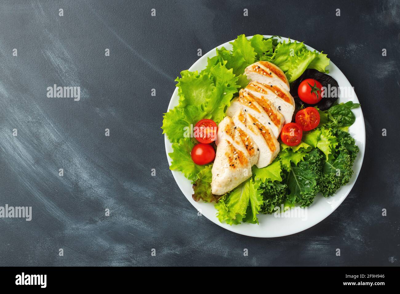 Filetto di petto di pollo e insalata di verdure con pomodori e foglie verdi su sfondo nero. Il concetto di cibo sano e dieta del keto. Vista dall'alto Foto Stock