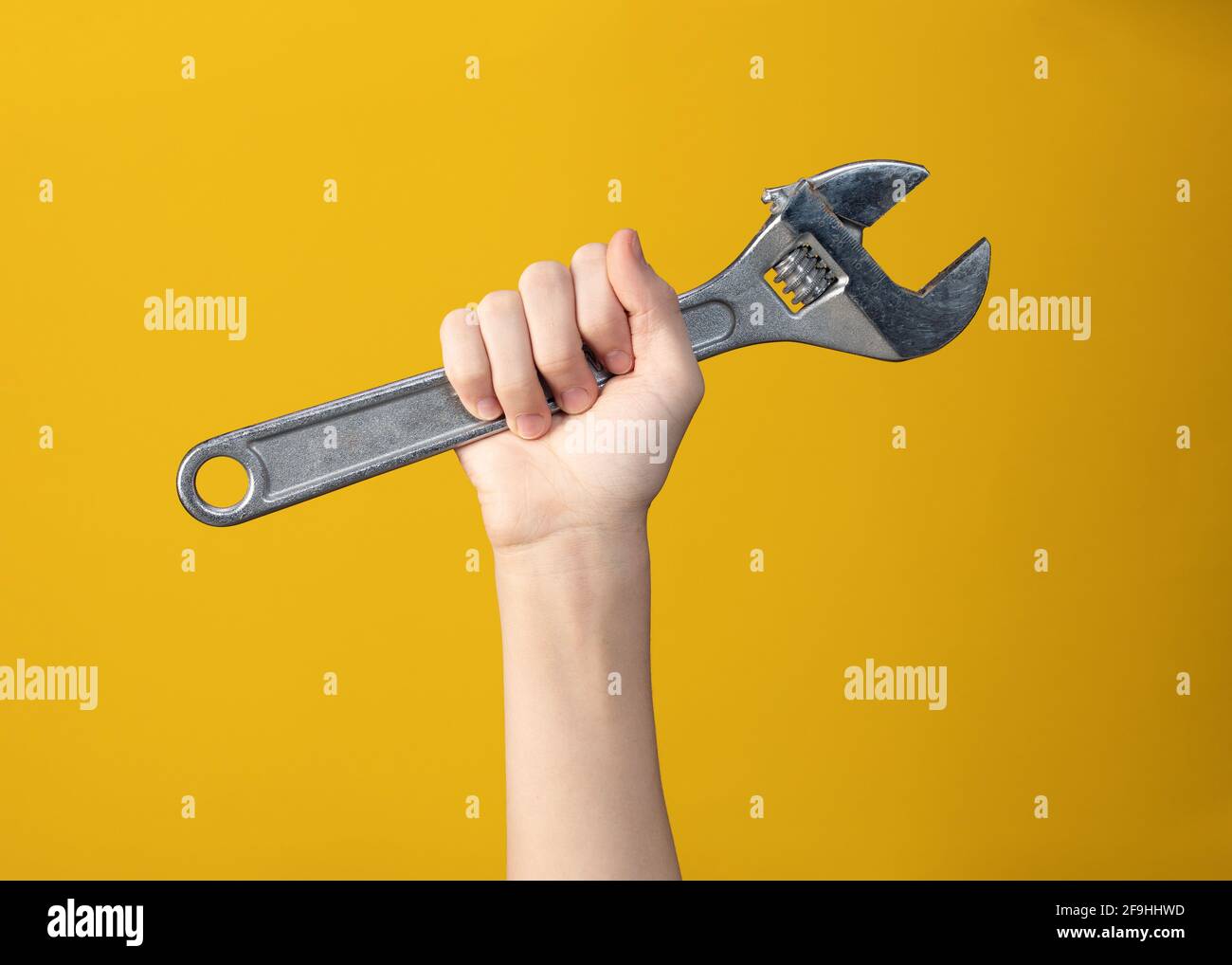 Primo piano di una grande chiave in acciaio in mano a un uomo su sfondo giallo. Attrezzo per la riparazione o la costruzione. Symbol è pronto per l'uso o poster del wor Foto Stock