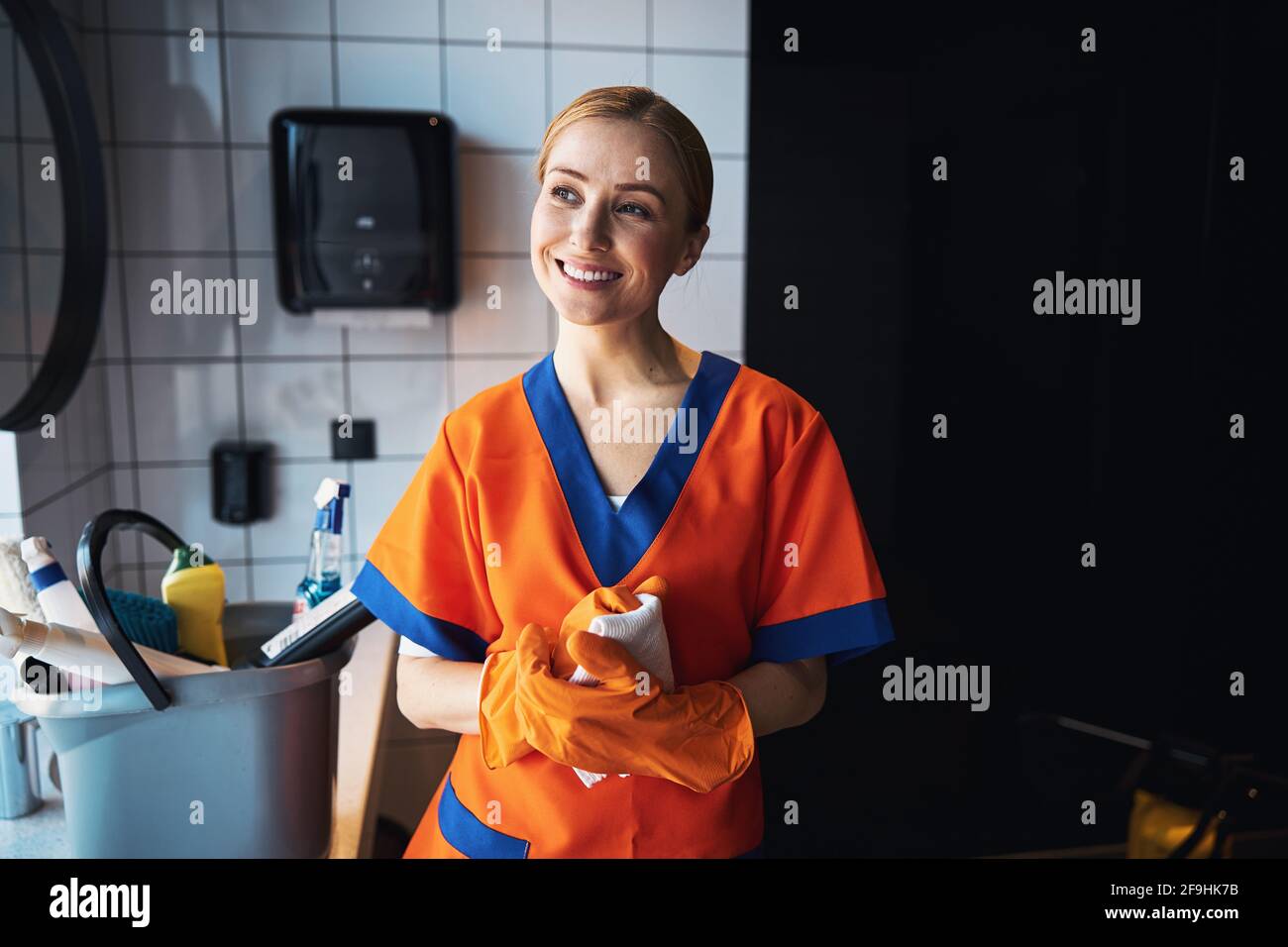 Sorridente padrona di casa per la pulizia che sogna nel bagno d'ufficio Foto Stock