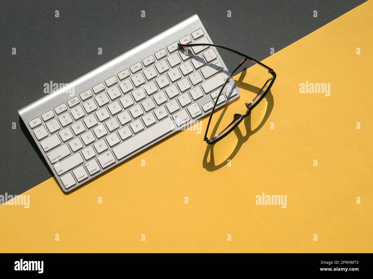 Tastiera bianca e occhiali da lettura su fondo giallo e nero. Disposizione piatta. Foto Stock