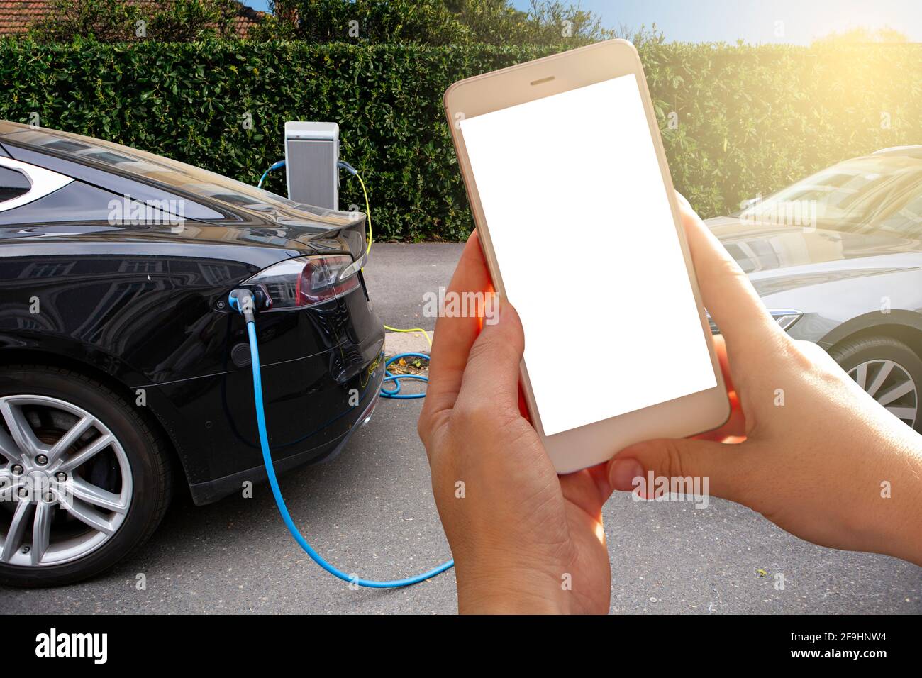 Mani con lo smartphone sullo sfondo di un'auto a noleggio presso la stazione di ricarica per i veicoli elettrici. Condivisione dell'auto. Foto Stock