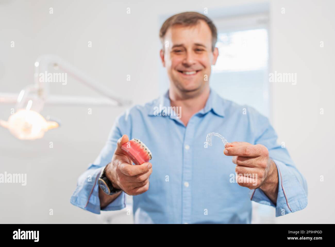 Dental care.smiling medico ortodontista che tiene aligners e bretelle in mano mostra la differenza tra loro Foto Stock