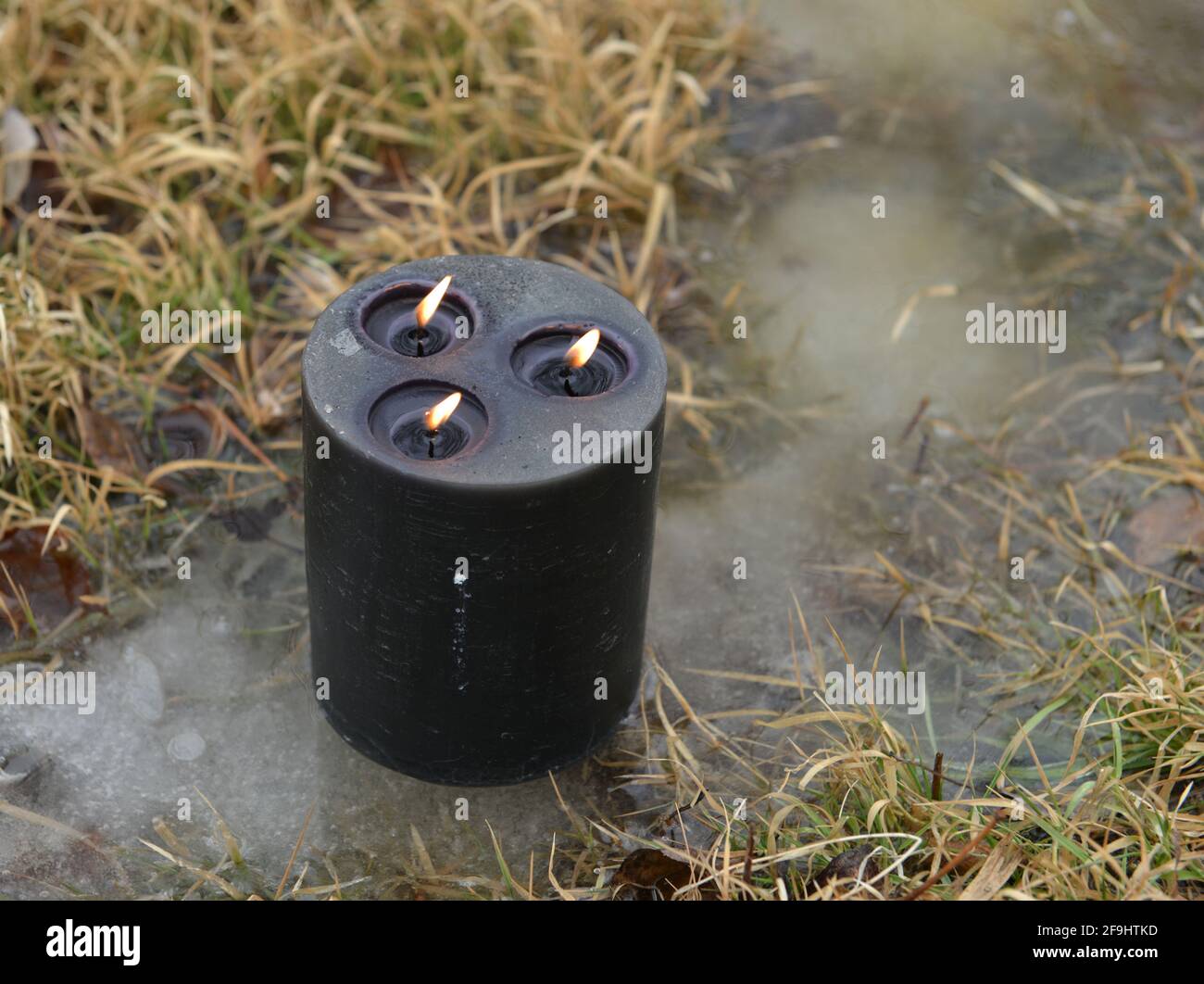 Candela nera che brucia in acqua all'esterno, rituale magico di wiccan. Sfondo esoterico, gotico e occulto, Halloween mistico e wicca concetto all'aperto. Foto Stock
