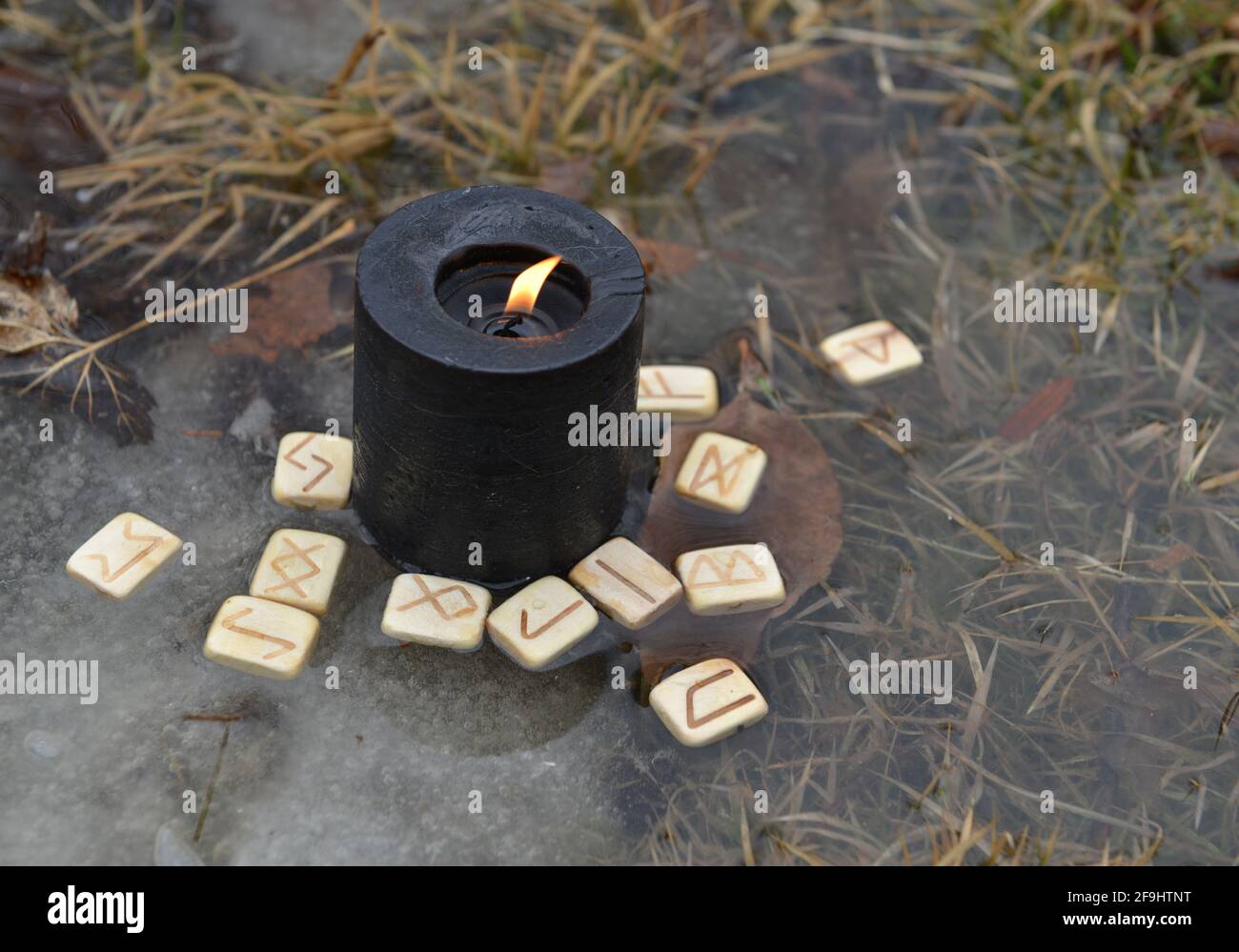 Rituale magico con candela nera e rune di legno nell'acqua esterna. Sfondo esoterico, gotico e occulto, Halloween mistico e wicca concetto outd Foto Stock