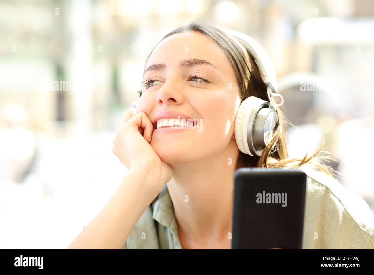 Donna felice che indossa le cuffie e tiene in mano uno smartphone che ascolta alla musica che sogna in una caffetteria Foto Stock