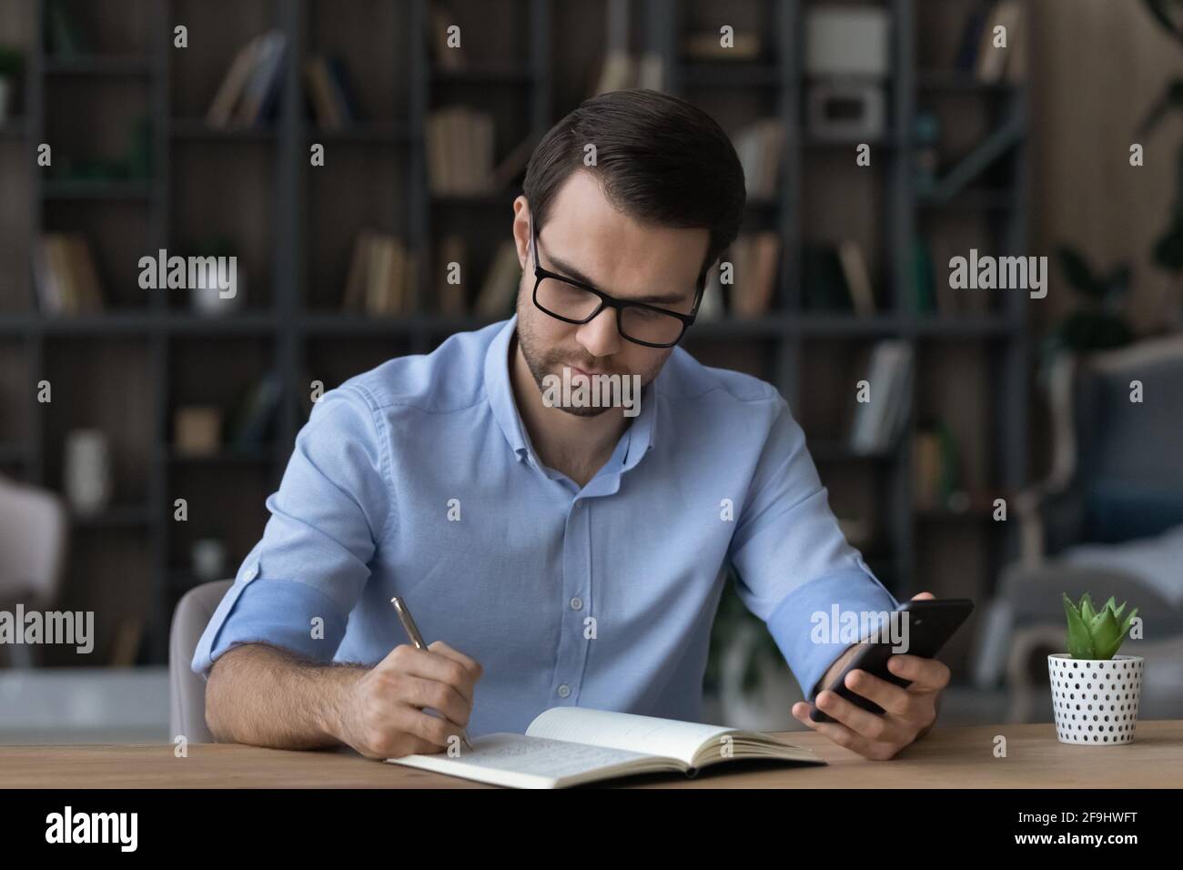 L'uomo pensivo usa la lista di fare del cellulare nel notebook Foto Stock
