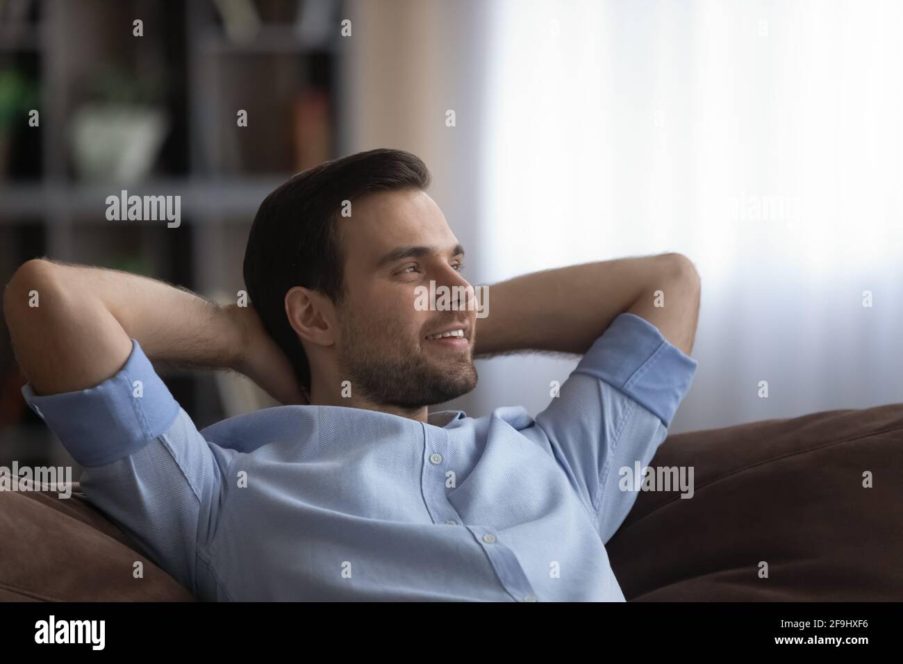 Uomo sorridente rilassarsi a casa sognando guardando in lontananza Foto Stock