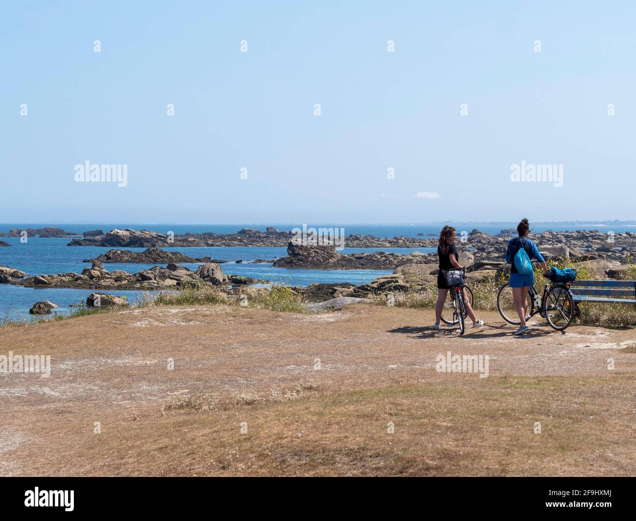 Due giovani donne in moto, di fronte al mare, costa rocciosa, nord Finistère, Bretagna, Francia. Foto Stock