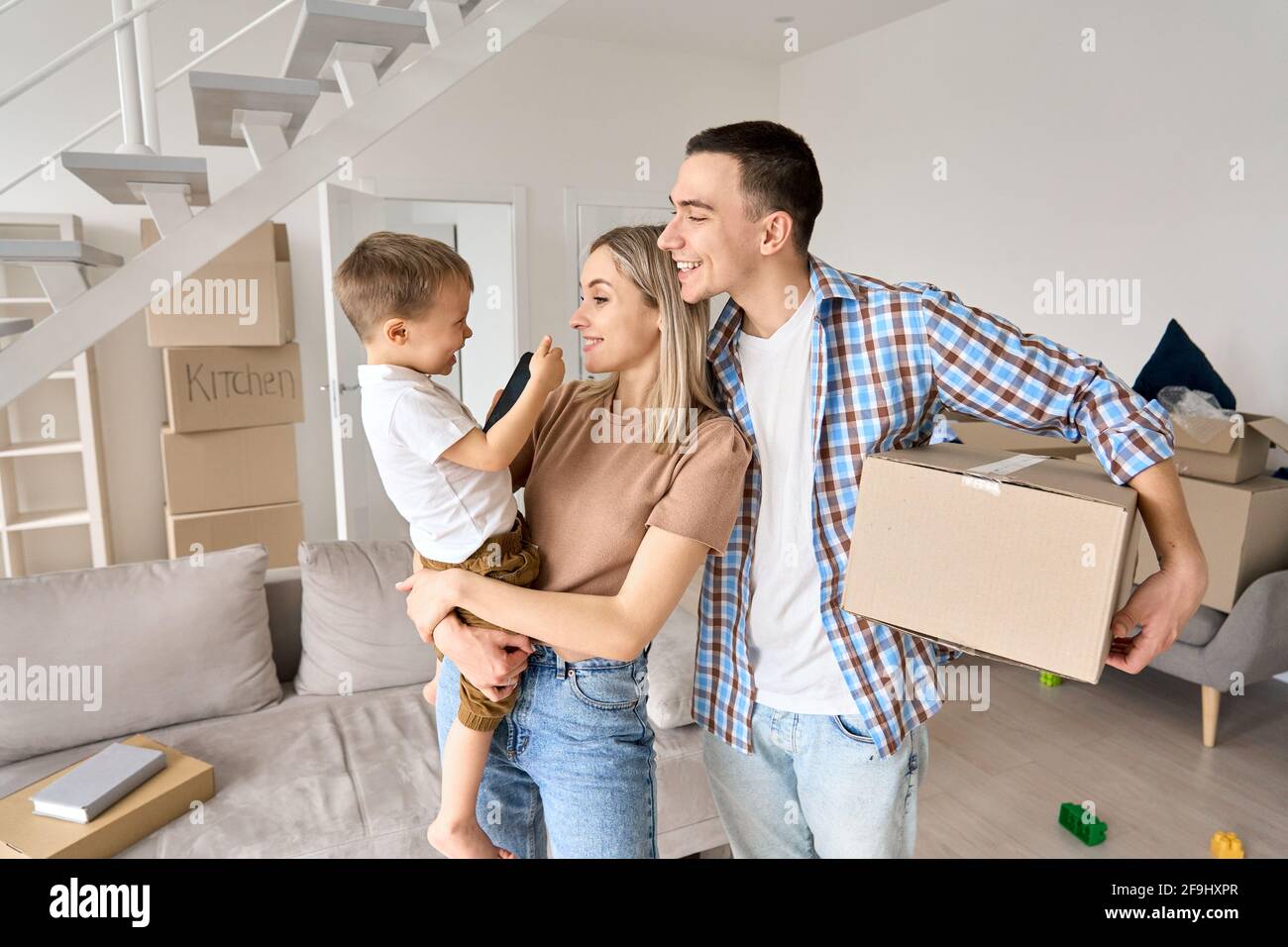 Famiglia felice nuovi proprietari domestici che tengono il figlio e la scatola del bambino sul giorno in movimento. Foto Stock