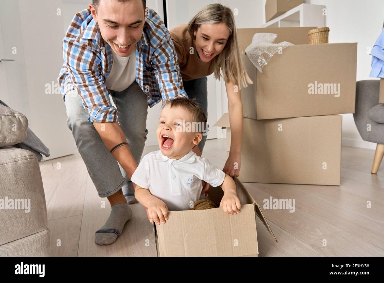 I genitori felici giocano con il figlio carino del bambino che cavalca nella scatola durante il giorno in movimento. Foto Stock