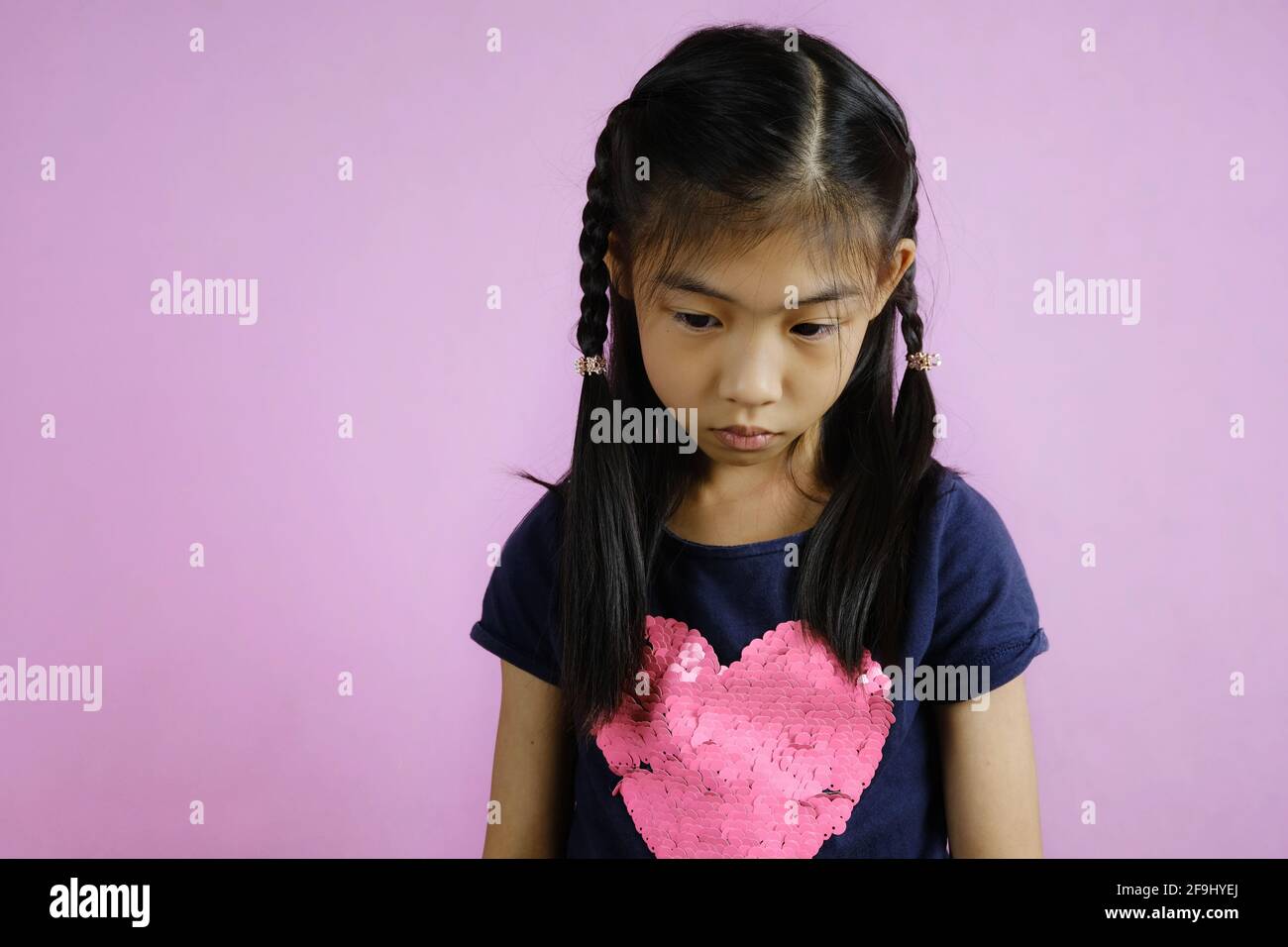 Un colpo di mezzo corpo di una ragazza asiatica carina giovane che guarda giù, sentendosi sconvolto, contemplando la sua azione seguente. Sfondo rosa brillante. Foto Stock