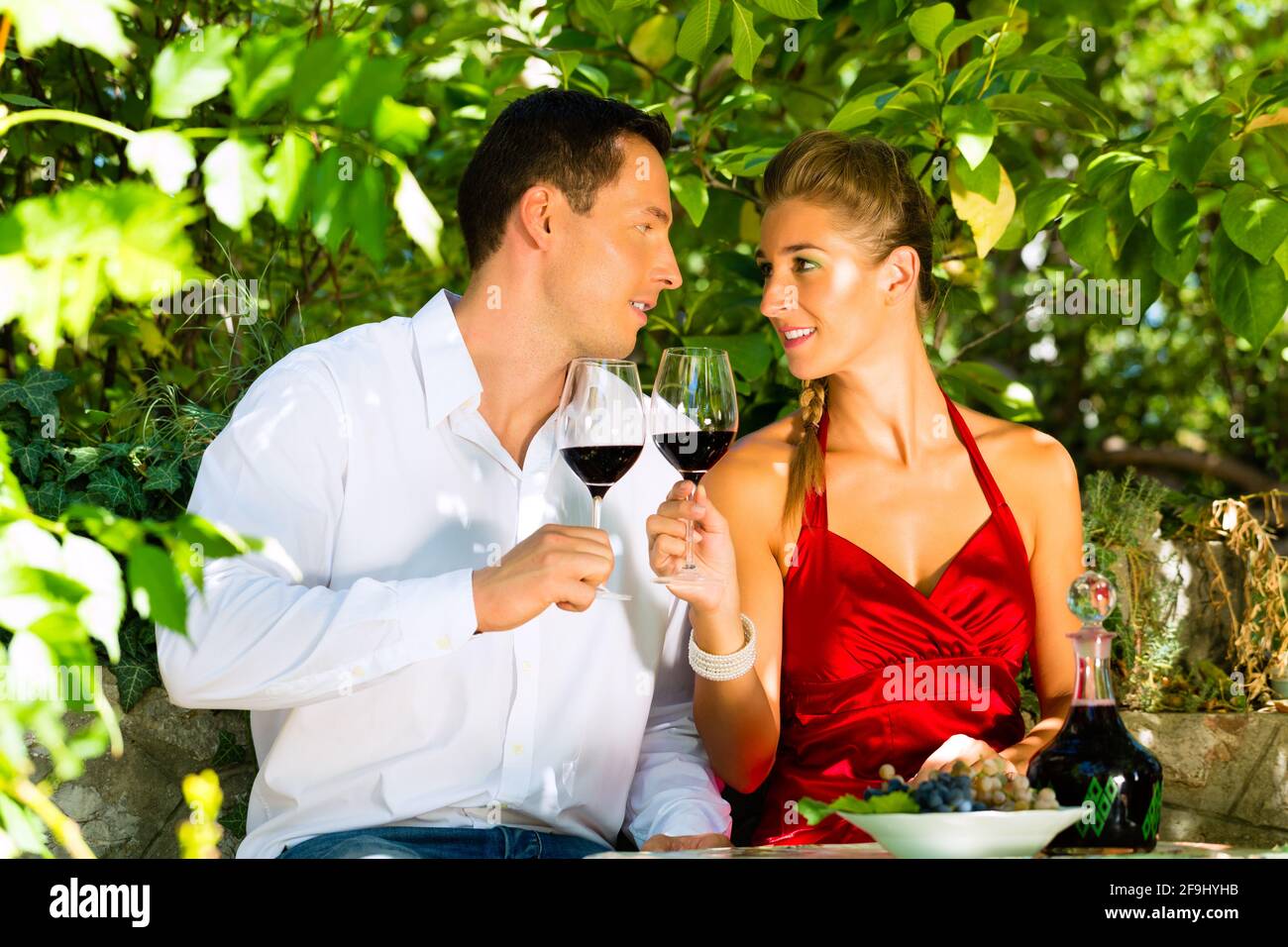 Donna e uomo seduto romanticamente sotto grapevine e bere il vino da un vetro Foto Stock