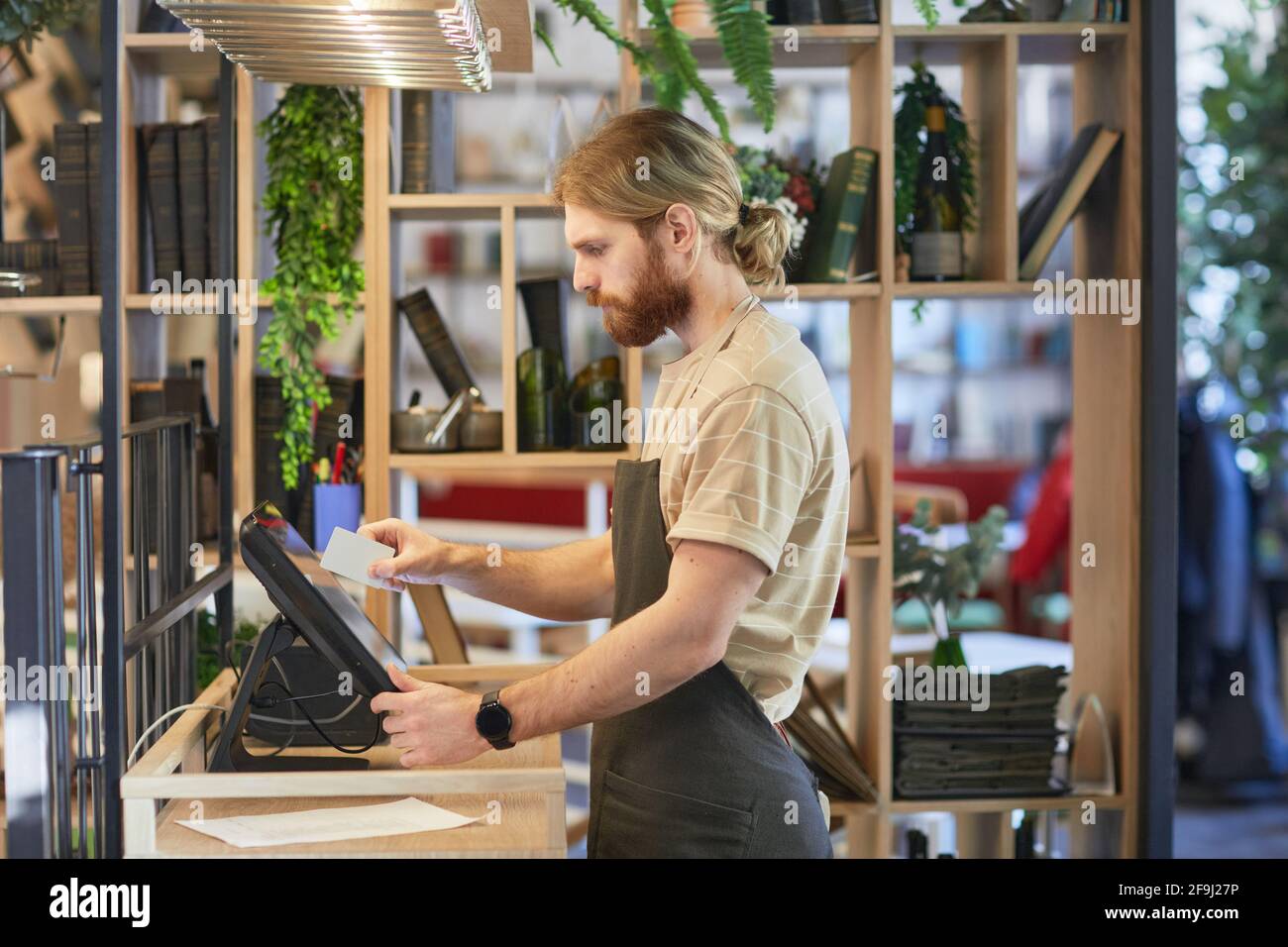 Vista laterale ritratto del lavoratore di caffè con portatore utilizzando registro durante l'elaborazione degli ordini in verde eco friendly interni, spazio di copia Foto Stock