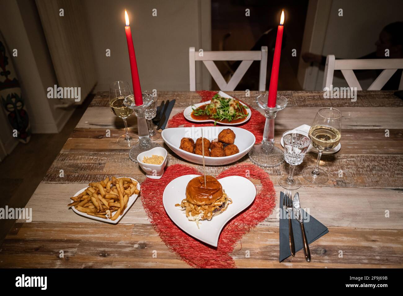Cena di San Valentino con cena romantica per due tavoli in legno a lume di  candela a forma di cuore rosso con Burger e Pasta Foto stock - Alamy