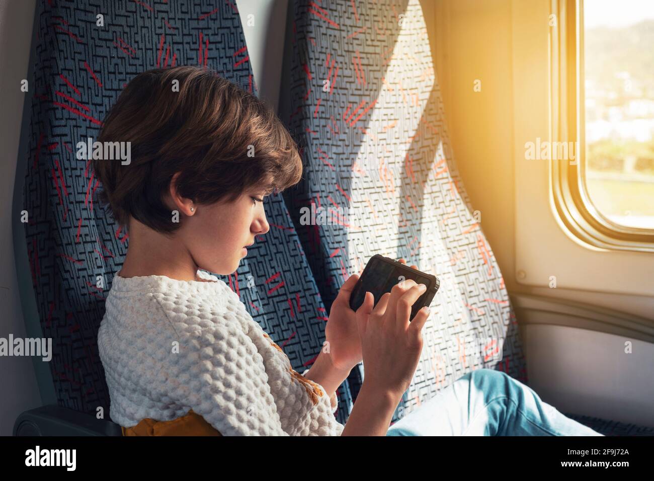 Ragazza di dieci anni che gioca al telefono su un treno in una giornata di sole. Foto Stock