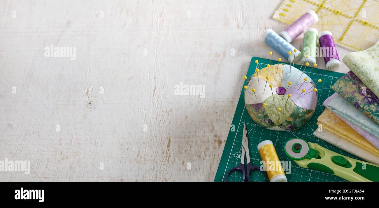 Pincushion, pila di tessuti, accessori per cucire e trapuntare giacenti su un tappetino da taglio, spazio per il testo Foto Stock