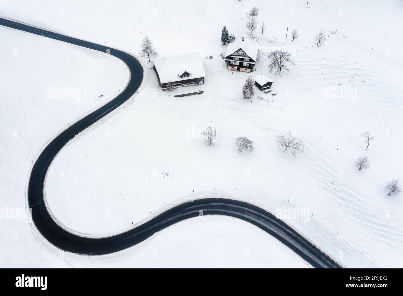 Strada che si snoda intorno a un villaggio innevato sulle Alpi svizzere in inverno, Svizzera Foto Stock