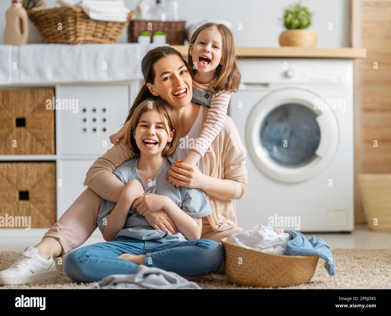 Bella giovane donna e bambini ragazze aiutanti poco stanno avendo divertimento e sorridendo mentre facendo lavanderia a casa. Foto Stock
