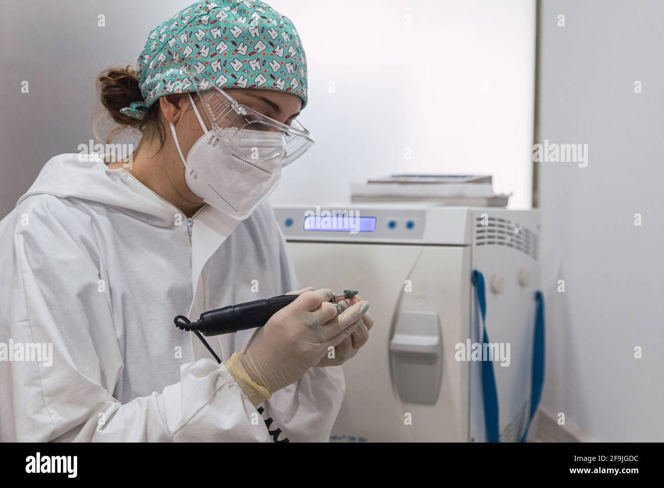 Mani di un tecnico dentale con maschera chirurgica e vetri che lucidano le protesi sulla sua tabella. Concetto di salute Foto Stock