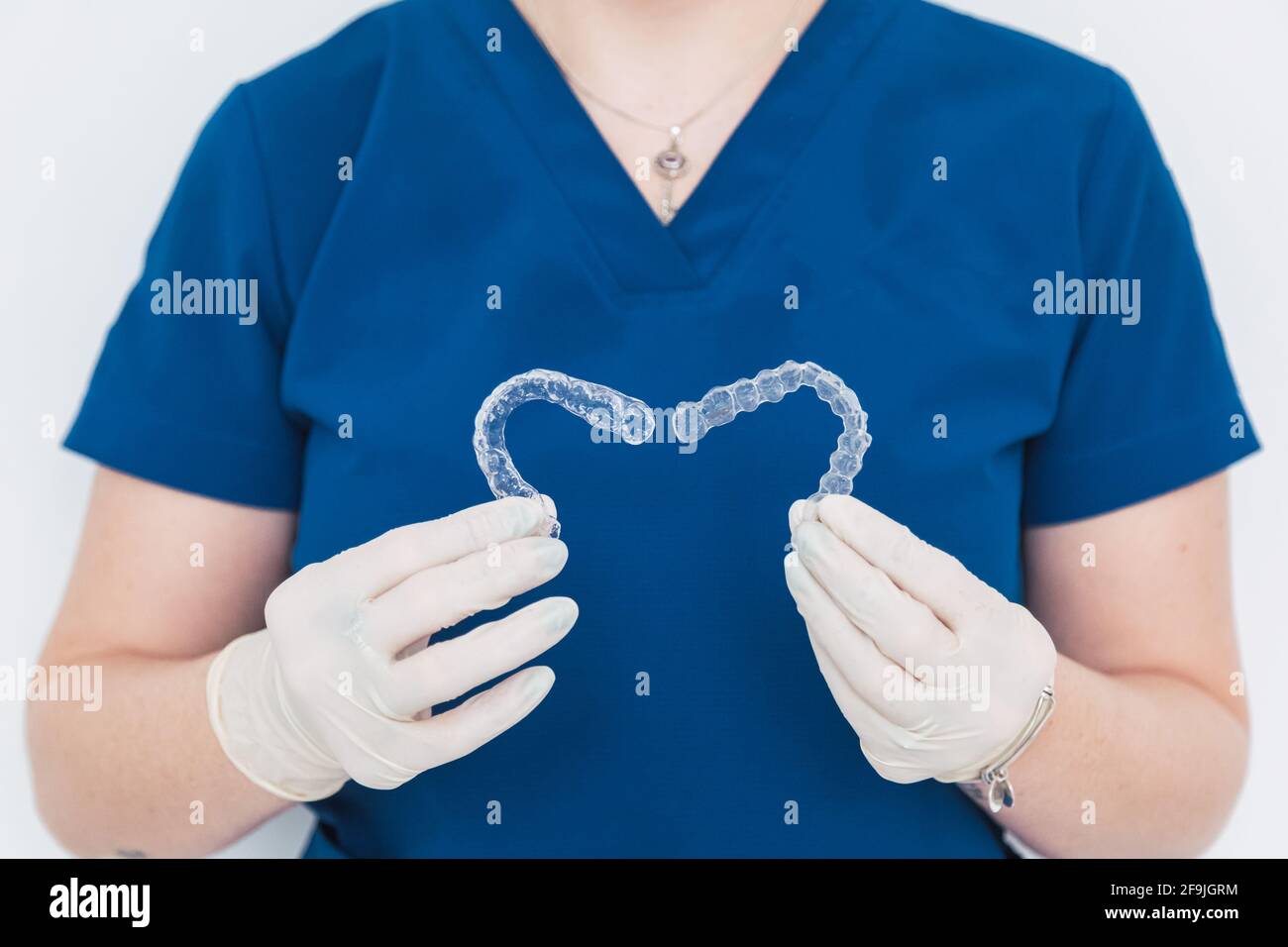 Medico irriconoscibile che tiene due allineatori dentali trasparenti a forma di cuore. Foto Stock