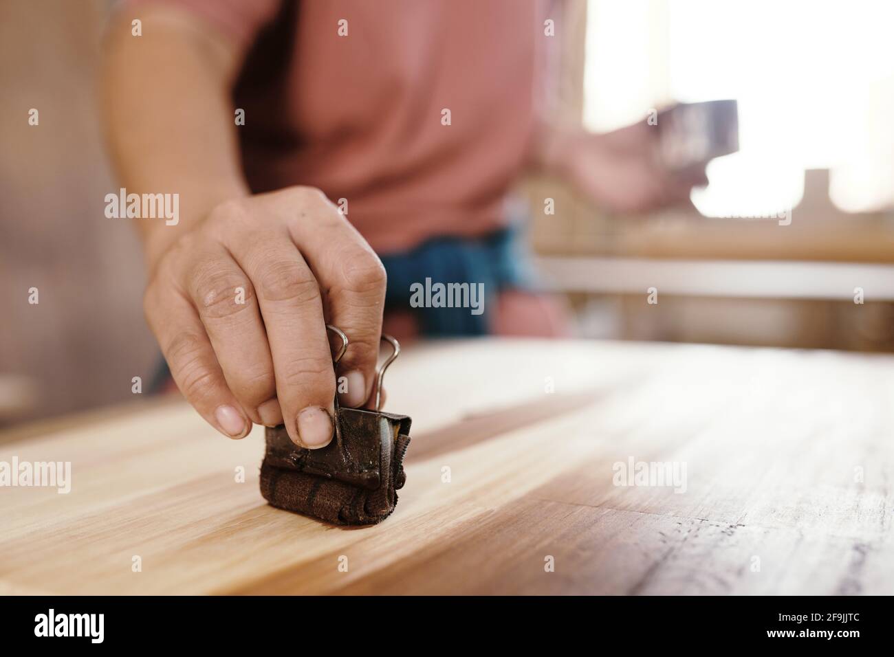 Immagine ravvicinata del carpentiere utilizzando una graffetta per rilegatura con pezzo di panno imbevuto di olio per coprire la superficie di legno Foto Stock
