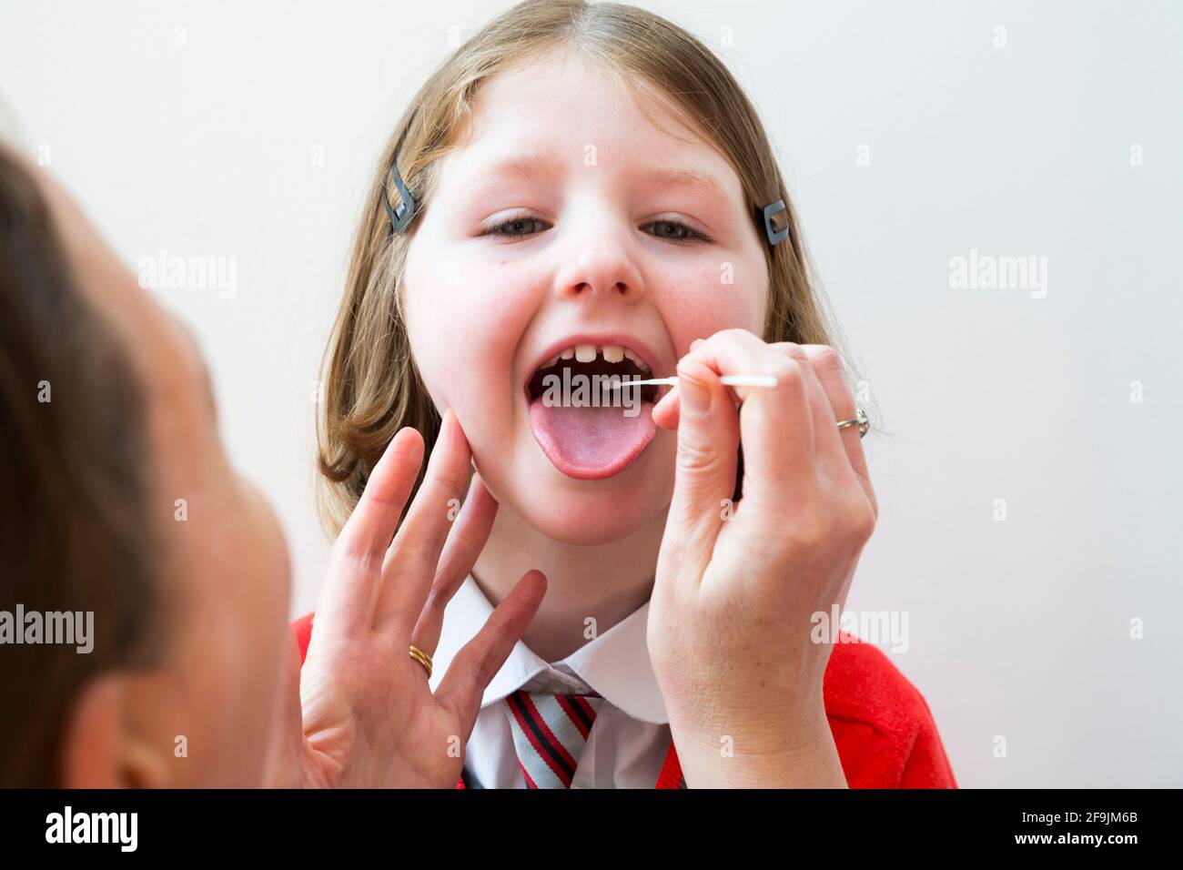 Età scolastica bambino scuola primaria ragazza di sei anni / 6 anni che ha campioni prelevati dalla gola per l'uso in un LFT di prova di flusso laterale dalla società cinese Innova. Inghilterra Regno Unito. (123) Foto Stock