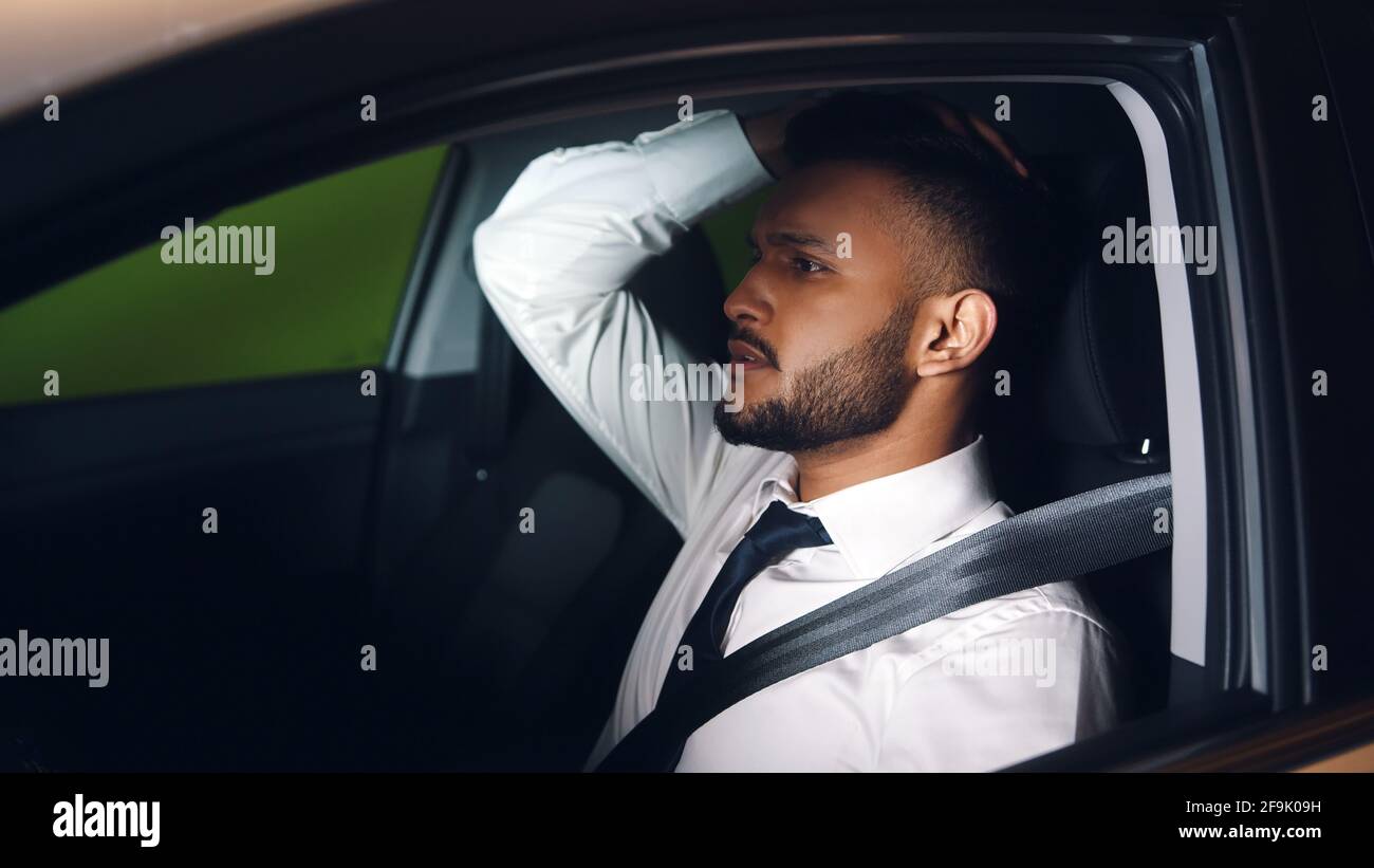 Uomo d'affari in camicia bianca seduto in macchina e tenendo la testa. Stressato e preoccupato uomo da corsa misto. Foto Stock
