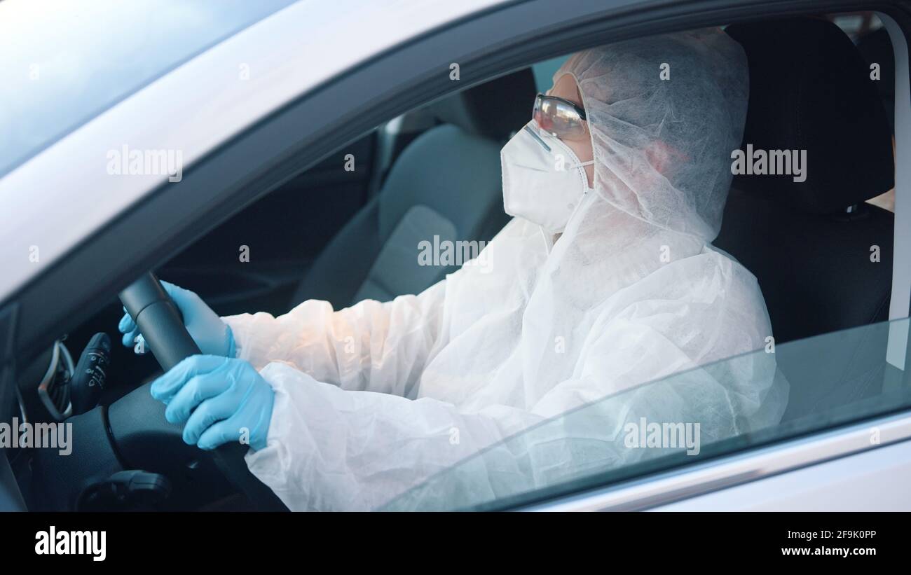 Persona non identificabile in tuta protettiva auto guida. Vista del finestrino laterale della vettura su uomo nell'area a rischio di infezione. Foto Stock