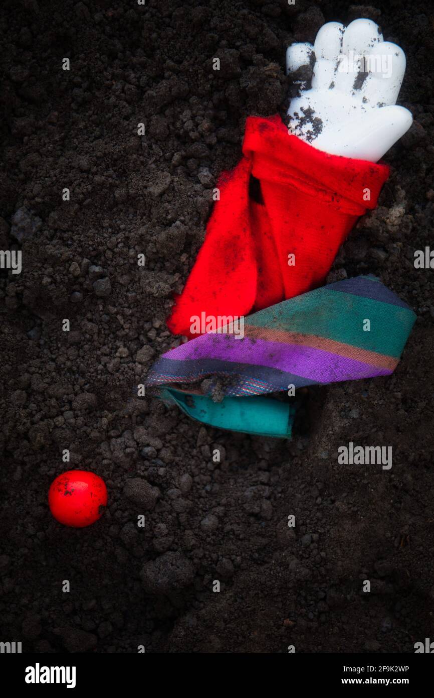 Pagliaccio sepolto nel terreno con mano, naso e abiti colorati sopra terra. Concetto di intrappolato, imprigionato, rapito Foto Stock
