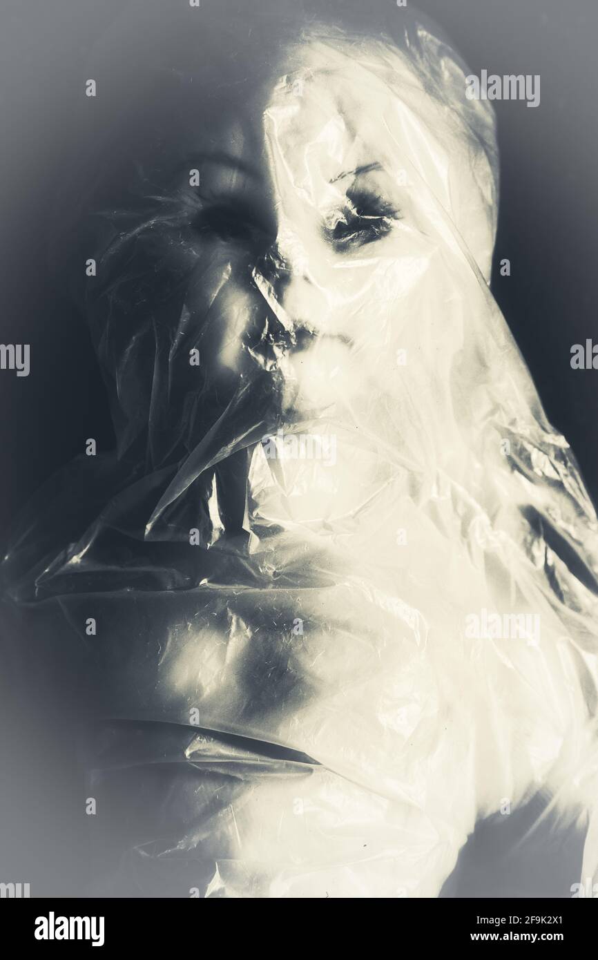 Primo piano bianco e nero di bambola femmina avvolta in plastica, concetto di intrappolato, rapito, cattività, claustrofobia Foto Stock