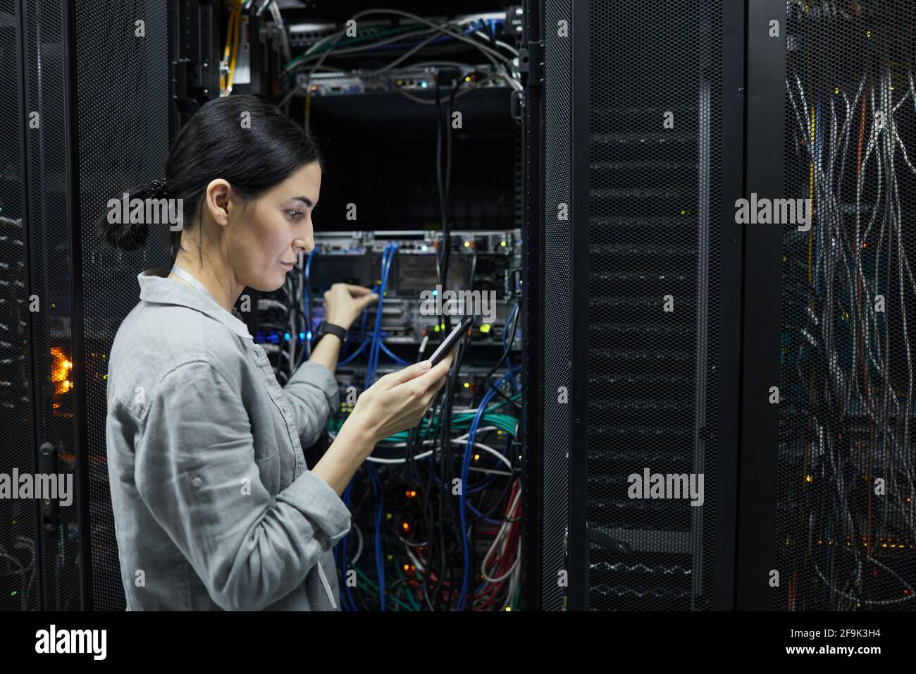 Vista laterale verticale del tecnico di rete femminile che collega i cavi nell'armadietto del server durante la configurazione del supercomputer nel data center, spazio di copia Foto Stock