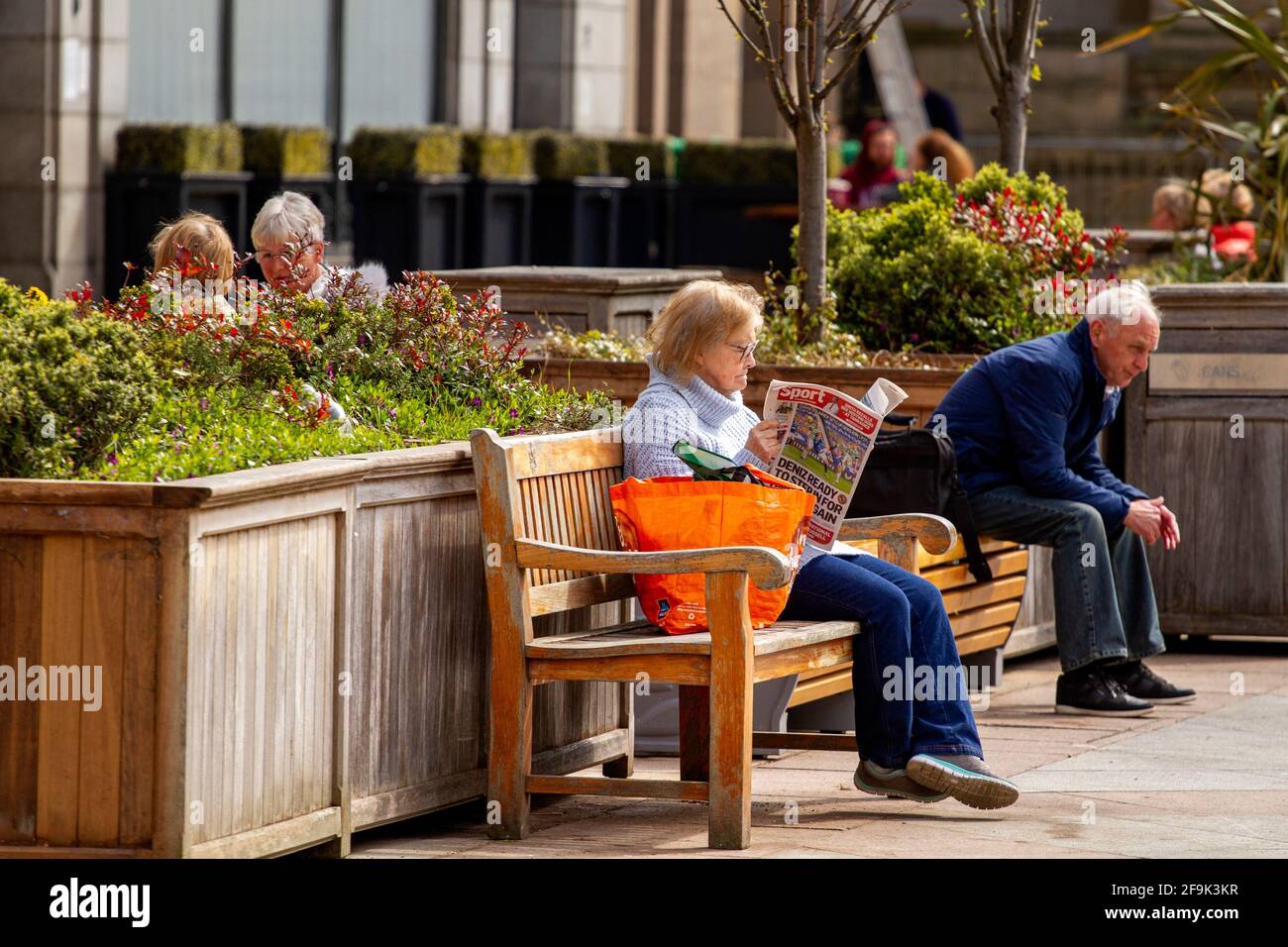 Dundee, Tayside, Scozia, Regno Unito. 19 Apr 2021. Regno Unito tempo: Bello caldo sole di primavera attraverso la Scozia nordorientale con temperature che raggiungono i 14°C. Il blocco Covid-19 si sta allentando con le persone che socializzano nel centro di Dundee, con alcuni negozi essenziali aperti. Una donna anziana si sta avvalendo delle nuove e rilassate norme di blocco e del clima soleggiato di aprile seduto su un sedile estivo leggendo il quotidiano locale Telegraph serale dopo una giornata di shopping. Credit: Dundee Photographics/Alamy Live News Foto Stock
