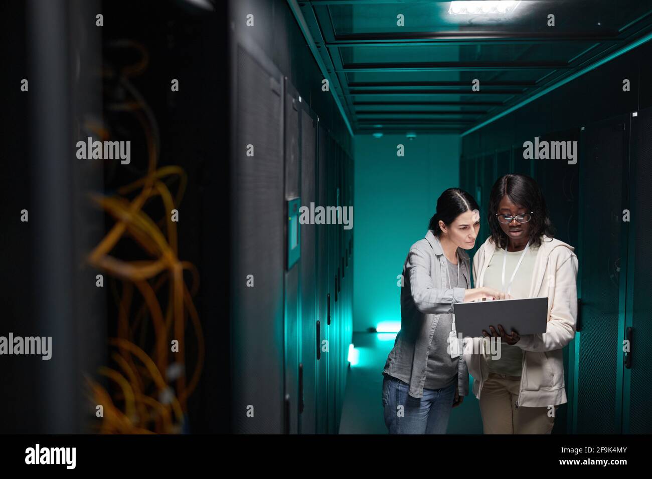 Ritratto grandangolare di due tecnici IT femminili che configurano la rete di server mentre lavorano nel data center, spazio di copia Foto Stock